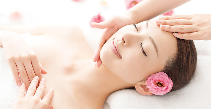 リラックスしている女性が、ヘッドマッサージを受けている様子。彼女の髪には花が飾られ、周囲には花弁が散らばっている。